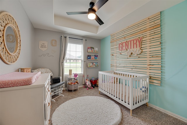 carpeted bedroom featuring a raised ceiling, ceiling fan, and a crib