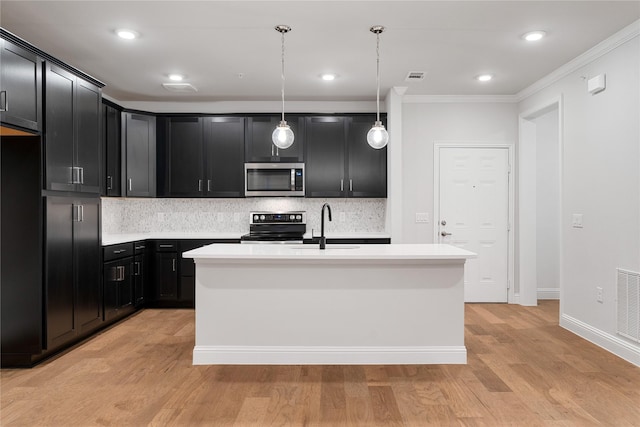 kitchen featuring hanging light fixtures, appliances with stainless steel finishes, a center island with sink, and backsplash