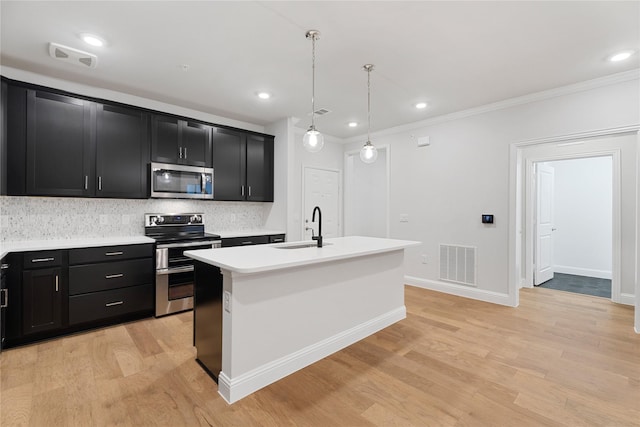 kitchen featuring hanging light fixtures, ornamental molding, appliances with stainless steel finishes, a kitchen island with sink, and light hardwood / wood-style floors