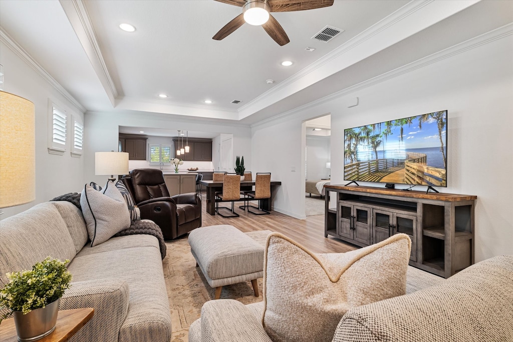 living room with light hardwood / wood-style flooring, ceiling fan, ornamental molding, and a tray ceiling