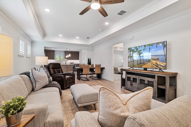 living room with light hardwood / wood-style flooring, ceiling fan, ornamental molding, and a tray ceiling