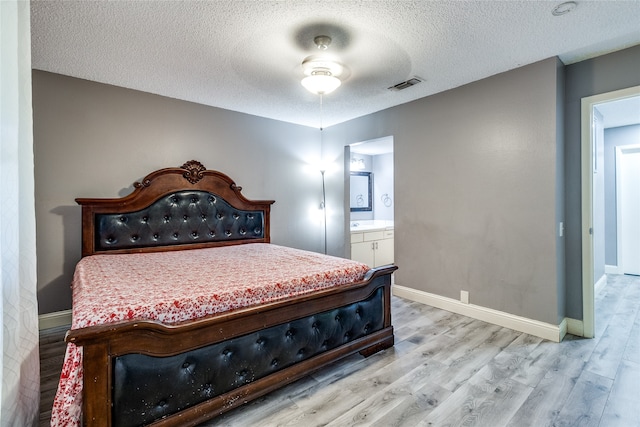 bedroom featuring ceiling fan, a textured ceiling, light hardwood / wood-style flooring, and ensuite bath