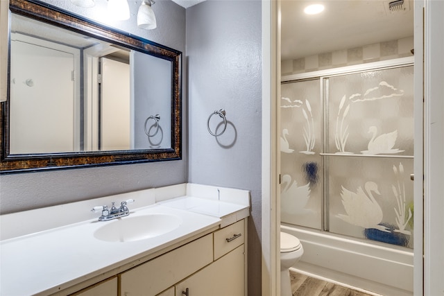 full bathroom featuring wood-type flooring, combined bath / shower with glass door, vanity, and toilet