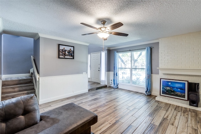 living room featuring light wood-type flooring, a textured ceiling, ceiling fan, and a brick fireplace