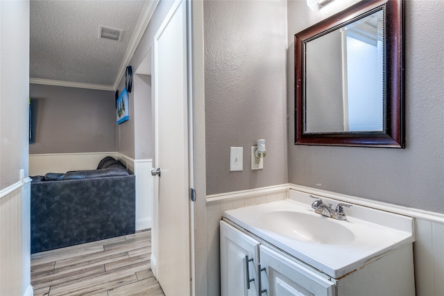 bathroom featuring vanity, a textured ceiling, ornamental molding, and wood-type flooring