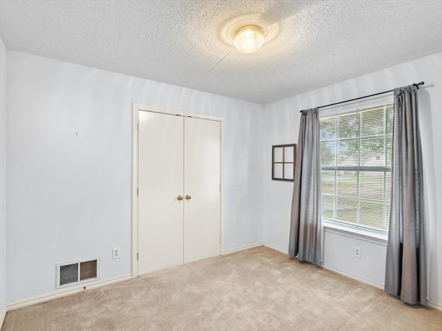 unfurnished bedroom featuring a textured ceiling, light colored carpet, and a closet