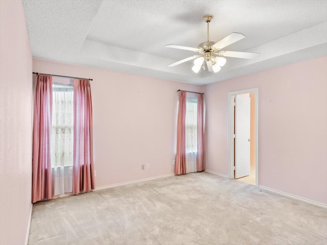 empty room with a raised ceiling, light colored carpet, a healthy amount of sunlight, and ceiling fan