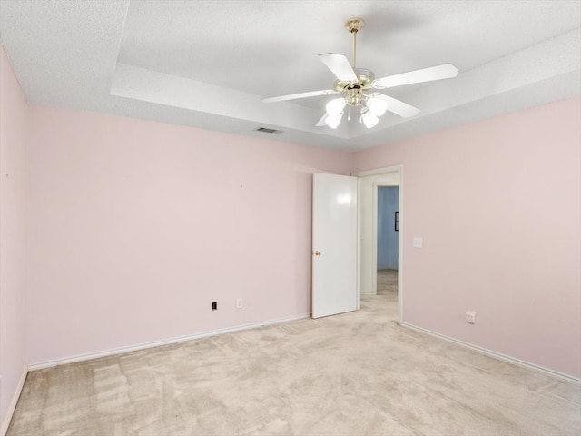 unfurnished room with a raised ceiling, light colored carpet, and ceiling fan