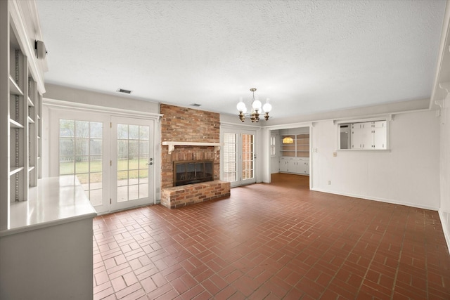 unfurnished living room with a chandelier, a textured ceiling, and a brick fireplace