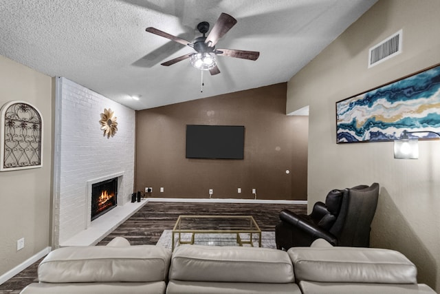 living room featuring vaulted ceiling, a large fireplace, hardwood / wood-style floors, ceiling fan, and a textured ceiling