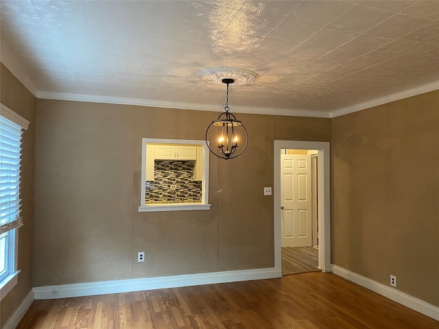 empty room with a notable chandelier, crown molding, baseboards, and wood finished floors