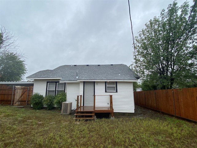 rear view of house featuring central air condition unit, roof with shingles, fence, and a lawn