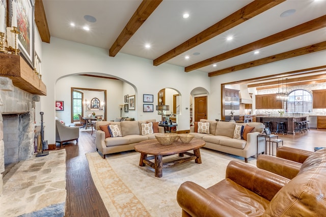 living room featuring a stone fireplace, beamed ceiling, a notable chandelier, and light hardwood / wood-style flooring