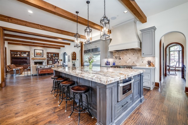 kitchen with gray cabinetry, dark hardwood / wood-style flooring, a large fireplace, and custom exhaust hood