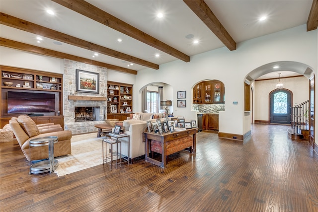 living room featuring built in features, dark hardwood / wood-style floors, beamed ceiling, and a stone fireplace