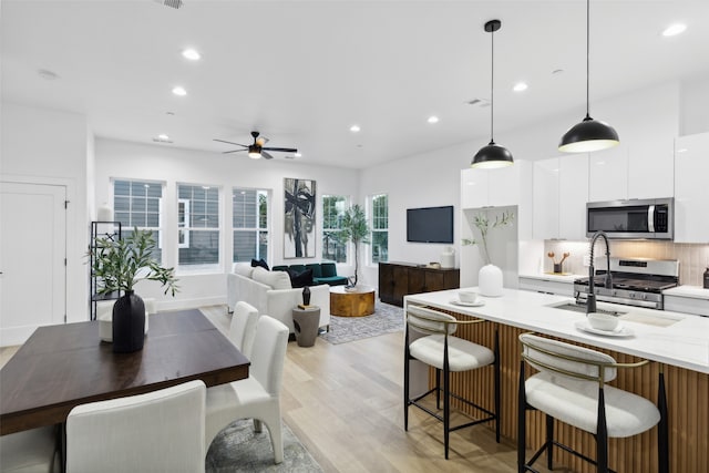 kitchen with decorative light fixtures, light stone countertops, appliances with stainless steel finishes, white cabinets, and light hardwood / wood-style floors