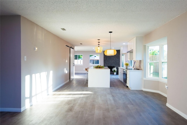 kitchen with a barn door, wood finished floors, a kitchen island, white cabinetry, and backsplash