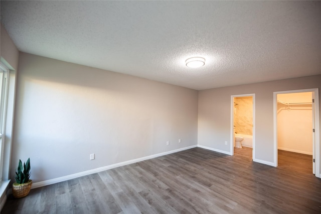 unfurnished bedroom featuring a textured ceiling, wood finished floors, baseboards, a spacious closet, and a closet