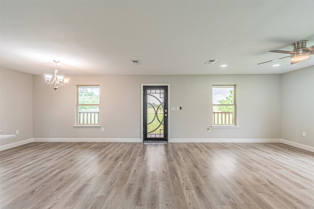 unfurnished room with plenty of natural light, ceiling fan with notable chandelier, and light hardwood / wood-style floors