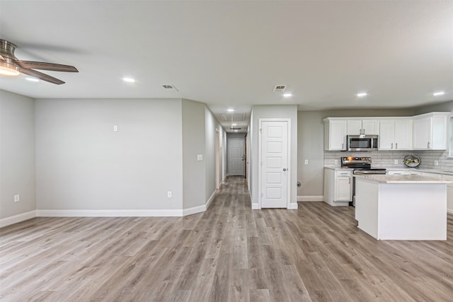 kitchen with light wood-type flooring, ceiling fan, decorative backsplash, appliances with stainless steel finishes, and white cabinets