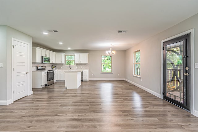 kitchen with white cabinets, hanging light fixtures, appliances with stainless steel finishes, wood-type flooring, and decorative backsplash