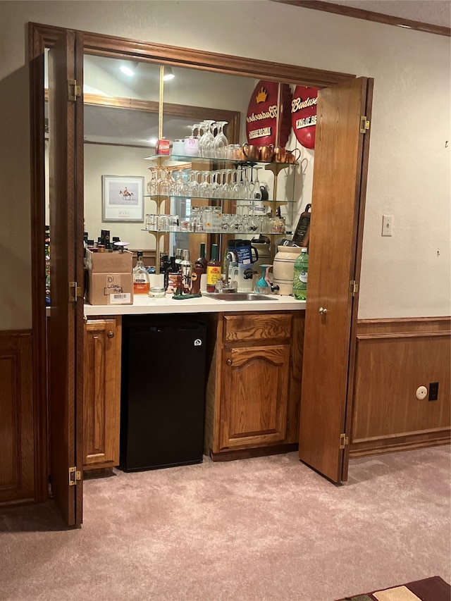 bar featuring sink, crown molding, light colored carpet, wooden walls, and black appliances