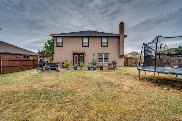 rear view of house featuring a patio, a lawn, and a trampoline