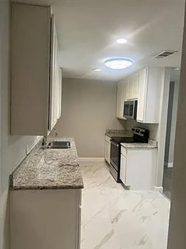 kitchen featuring white cabinets, light stone counters, stainless steel appliances, and sink