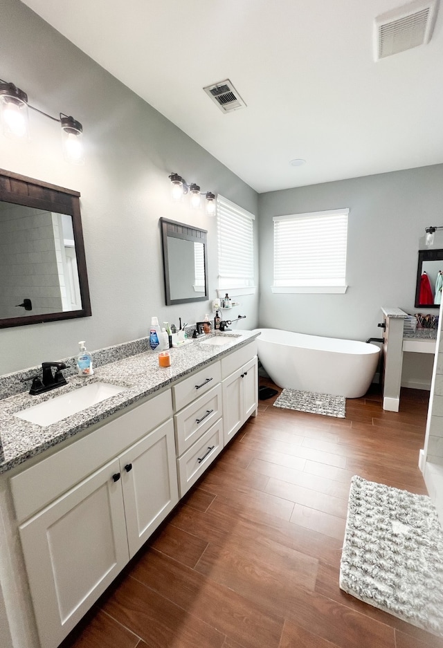 bathroom with a tub to relax in, vanity, and wood-type flooring