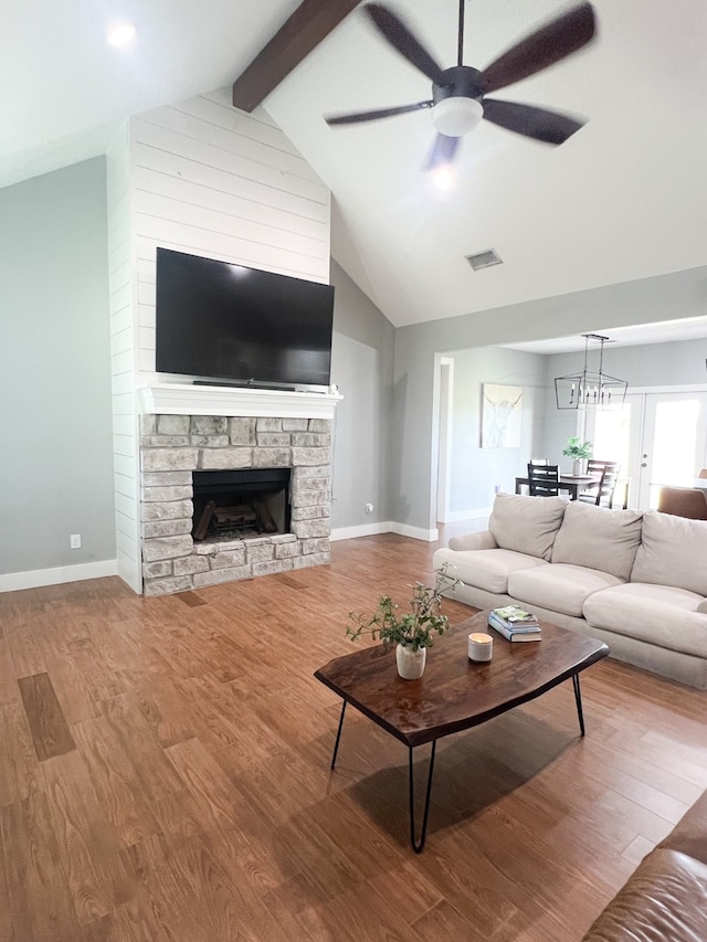 living room featuring ceiling fan, hardwood / wood-style flooring, beamed ceiling, and a stone fireplace