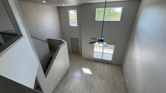 interior space with light wood-type flooring, ceiling fan, a textured ceiling, and a towering ceiling