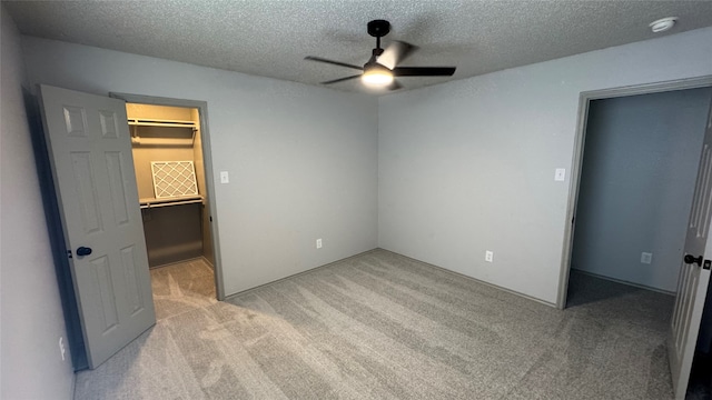 unfurnished bedroom featuring a textured ceiling, a walk in closet, a closet, light carpet, and ceiling fan