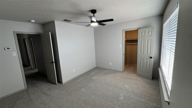 unfurnished bedroom with light colored carpet, a closet, a spacious closet, ceiling fan, and a textured ceiling