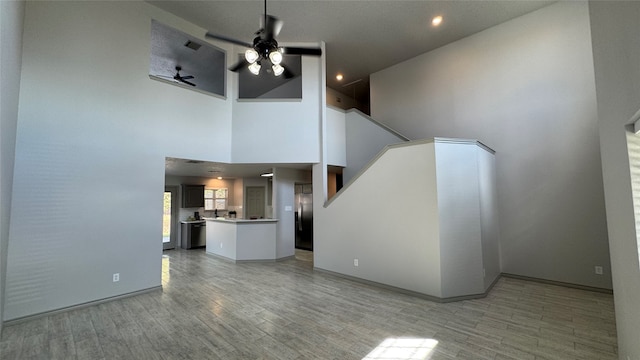 unfurnished living room featuring a high ceiling, ceiling fan, and light hardwood / wood-style floors