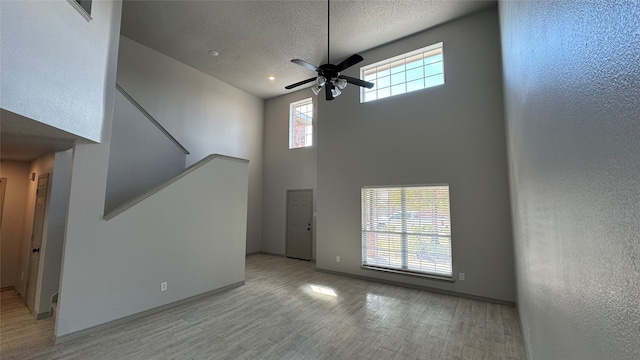 unfurnished living room with a high ceiling, ceiling fan, and light hardwood / wood-style floors