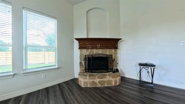 unfurnished living room featuring baseboards, dark wood finished floors, and a stone fireplace