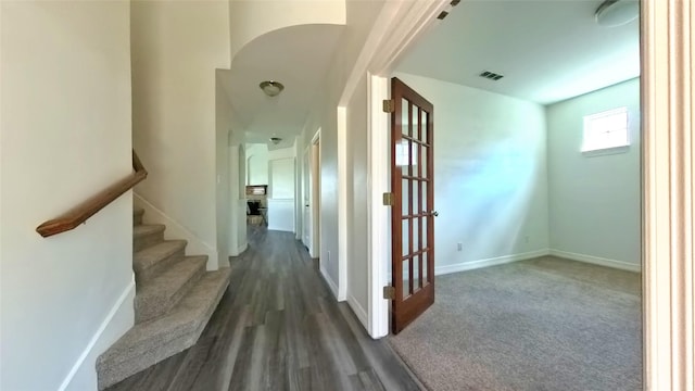 hallway featuring arched walkways, visible vents, baseboards, stairs, and dark wood finished floors