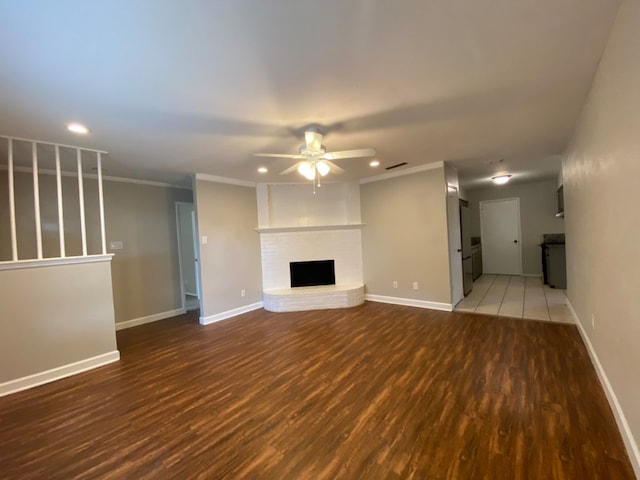 unfurnished living room featuring a fireplace, crown molding, hardwood / wood-style floors, and ceiling fan