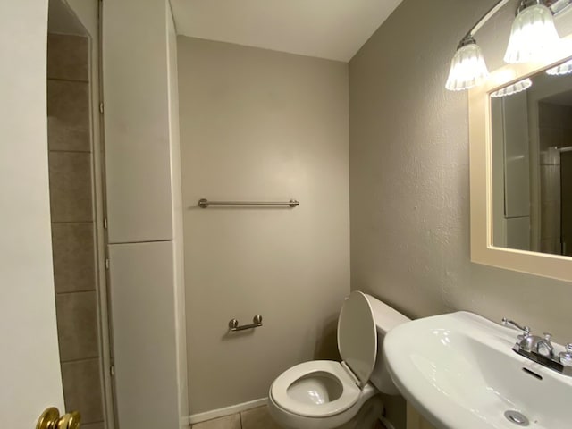 bathroom with tiled shower, tile patterned flooring, toilet, and sink