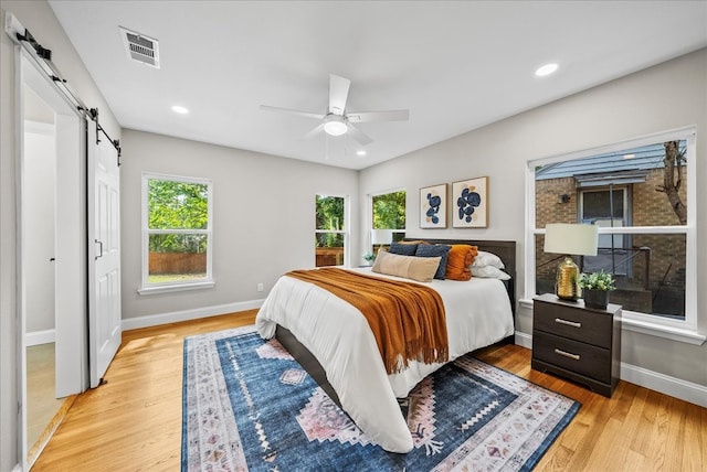 bedroom featuring a barn door, ceiling fan, and light hardwood / wood-style flooring