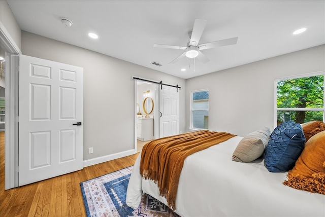 bedroom with a barn door, ceiling fan, light hardwood / wood-style flooring, and ensuite bathroom