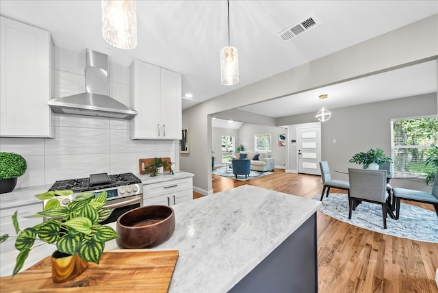 kitchen with white cabinets, pendant lighting, wall chimney exhaust hood, and light hardwood / wood-style flooring