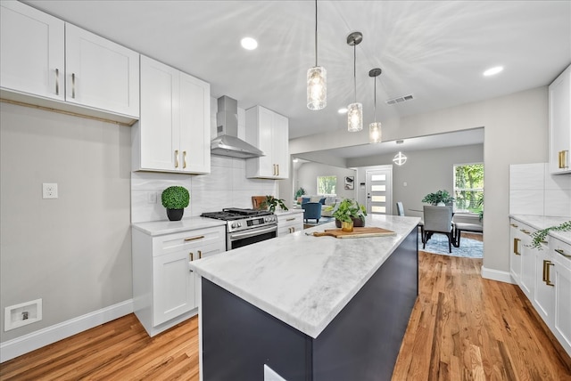 kitchen featuring hanging light fixtures, gas stove, light wood-type flooring, white cabinetry, and wall chimney exhaust hood