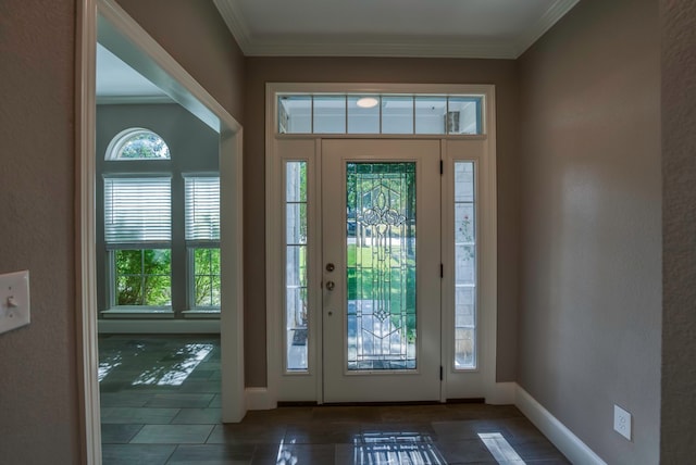 foyer with a wealth of natural light, dark tile patterned floors, and crown molding