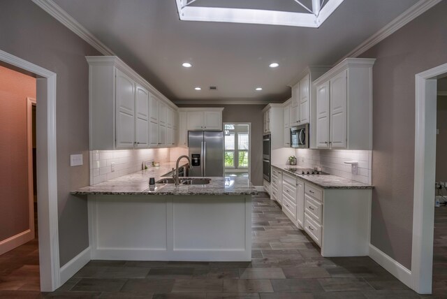 kitchen with light stone countertops, stainless steel appliances, white cabinetry, sink, and kitchen peninsula