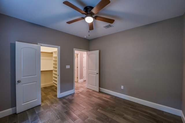 unfurnished bedroom featuring dark wood-type flooring, a walk in closet, ceiling fan, and a closet