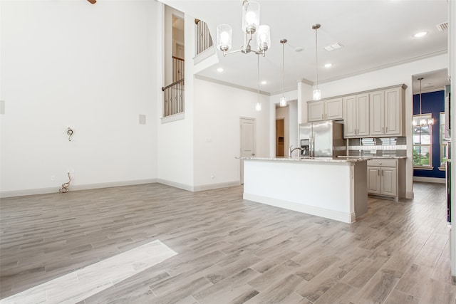 kitchen featuring stainless steel fridge with ice dispenser, an island with sink, decorative light fixtures, and light hardwood / wood-style floors