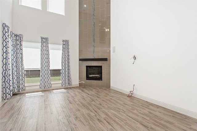 unfurnished living room featuring a tile fireplace, a high ceiling, and light hardwood / wood-style floors