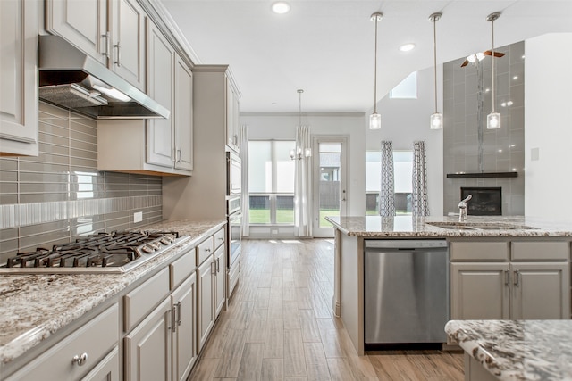 kitchen featuring pendant lighting, stainless steel appliances, light stone countertops, and light hardwood / wood-style floors