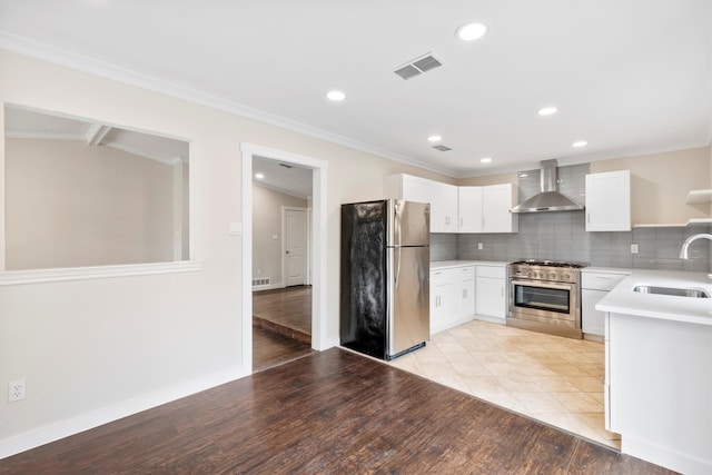 kitchen featuring stainless steel appliances, sink, white cabinetry, wall chimney range hood, and light wood-type flooring